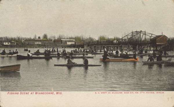 Text on front reads: "Fishing Scene at Winneconne, Wis." Many boats with men and women fishing are near the Main Street bridge over the Wolf River. The city of Winneconne is located on both sides of the Wolf River that flows between Lake Winneconne and Lake Butte des Morts.