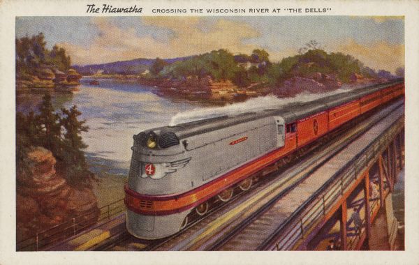Text on front: "The Hiawatha. Crossing the Wisconsin River at the 'Dells'." On reverse: "The Scenic Route. The Milwaukee Road is the only double tracked route all the way between Chicago and the Twin Cities. It is the scenic route through beautiful lakelands, the picturesque Wisconsin Dells, and for 140 miles along the Mississippi River. Four Hiawathas provide Double Daily Service. No extra fare." The Hiawatha locomotive #4 and passenger cars travel over the bridge at the Wisconsin Dells. The Wisconsin River, rock formations and trees fill the background. The Hiawatha route ran from 1935 to 1971.
