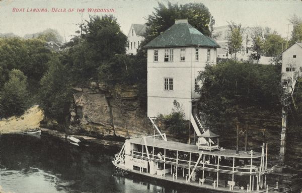 Text on front reads: "Boat Landing, Dells of the Wisconsin." The steamboat "Apollo No. 1" at the Dells Boat Landing on the Wisconsin River. A building and trees are perched on the rock formation on the shoreline of the river with more buildings in the background.