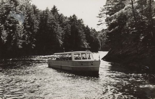 Tourists on the "Commander", a Wisconsin Dells tour boat on the Wisconsin River. The shores are lined with rock formations and trees.