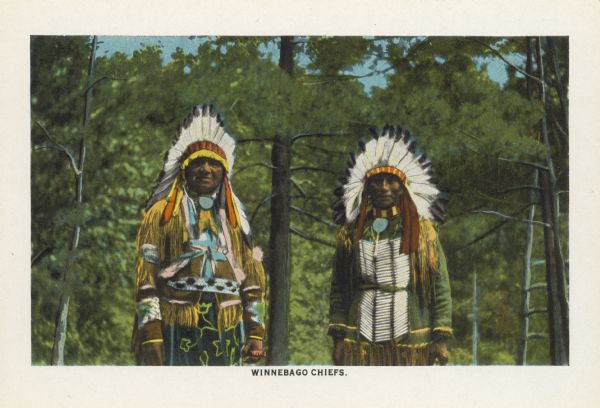 Text on front reads: "Winnebago Chiefs." One of 16 postcard images inside of a souvenir view folder. Two Native American Chiefs wearing indigenous clothing, are poinge with pine trees in the background. 