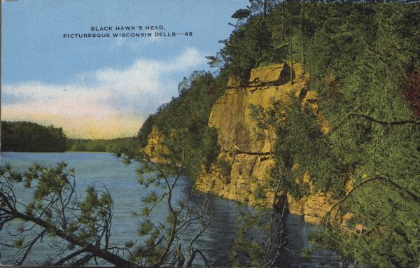 Text on front reads: "Black Hawk's Head, Picturesque Wisconsin Dells." On reverse: "Perhaps in no other place in America does Nature offer such a lavish array of natural wonders as in the Wisconsin Dells. Black Hawk's Head, or Great Stone Face as the Indians first named it, is an interesting example of Nature's ability as a sculptor. If you look closely you will see an almost perfect profile of a human head." A rock formation on the bank of the tree-lined Wisconsin River.