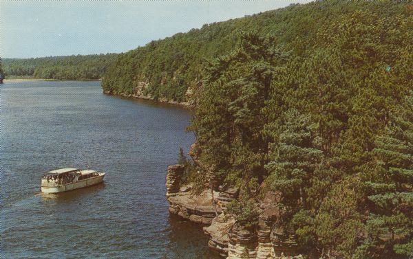 Text on front reads: "The Wisconsin at Chimney Rock, Wisconsin Dells, Wis." A tour boat full of visitors on the Wisconsin River at the formation named Chimney Rock. The shoreline is filled with more formations and trees.