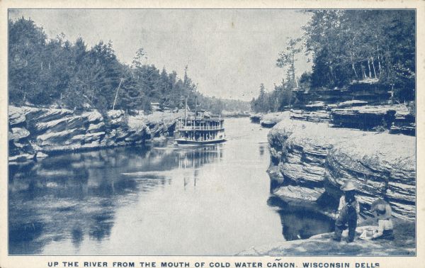 Text on the front reads: "Up the River from the Mouth of Cold Water Cañon, Wisconsin Dells." Two children are on a rock shelf on the lower right, gazing at a steamboat near the opposite bank in the distance. The shorelines of the Wisconsin River are lined with rock formations and trees.
