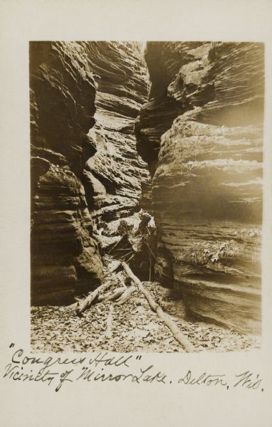 Handwritten on front: "'Congress Hall.' Vicinity of Mirror Lake. Delton Wis." View of a narrow passage through rock formations at Congress Hall, on the Dell View Resort property.