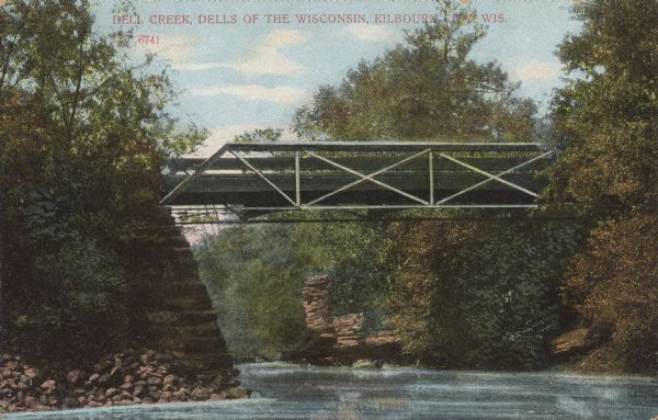 Text on front reads: "Dell Creek, Dells of the Wisconsin, Kilbourn City, Wis." A bridge over Dell Creek. Rock formations and trees line the shore. Dell Creek is a warm freshwater stream that lies in northeastern Sauk County and southern Juneau County in central Wisconsin. Impoundments on Dell Creek create Lake Delton and Mirror Lake. Dell Creek empties into the Wisconsin River.<p>Kilbourn City was founded in 1857 by Byron Kilbourn, the name was changed in 1931 to Wisconsin Dells.</p>