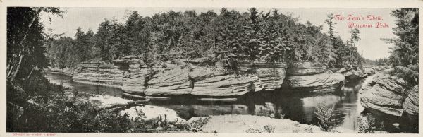 Text on front reads: "The Devil's Elbow, Wisconsin Dells." A panoramic view of the Devil's Elbow, with trees and rock formations lining the banks. A double wide "Souvenir Mail Card" that folds in half for mailing.