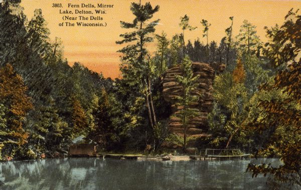 Text on front reads: "Fern Dells, Mirror Lake, Delton, Wis. (Near The Dells of The Wisconsin)." Rock formations, trees, boathouse, boat and dock on the shore of Mirror Lake.