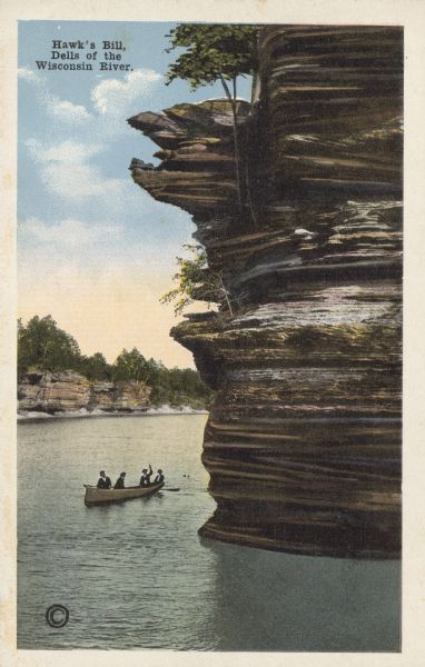 Text on the front reads: "Hawk's Bill, Dells of the Wisconsin River." Four men in a rowboat are beneath the Hawk's Bill rock formation. One man is pointing upward. Trees are clinging to the formations and growing above.