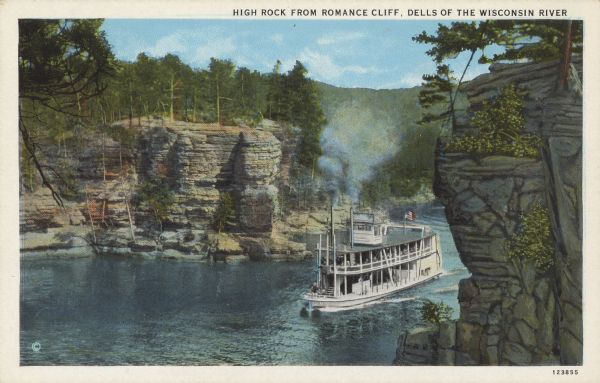 Text on front reads: "High Rock from Romance Cliff. Dells of the Wisconsin River." On reverse: "High Rock from Romance Cliff.–This is the imposing 'Lower Jaws of the Dells' named by the old raftsmen in the early days. These are the first high cliffs on the Upper Dells, and are a short distance above the city of Kilbourn." Elevated view looking down at an excursion boat steaming through past High Rock. Trees are clinging to the formations and growing on top.<p>Kilbourn City was founded in 1857 by Byron Kilbourn, the name was changed in 1931 to Wisconsin Dells.</p>