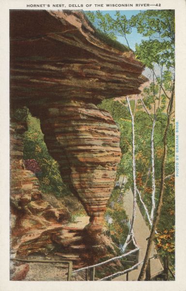 Text on front reads: "Hornet's Nest, Dells of the Wisconsin River." On reverse: "From Luncheon Hall to the right is the Hornet's Nest, a cone shaped rock, closely resembling a hornet's nest. It is the result of erosion by the elements during bygone times." The rock formation "Hornet's Nest" surrounded by a boardwalk, railings, trees and foliage.