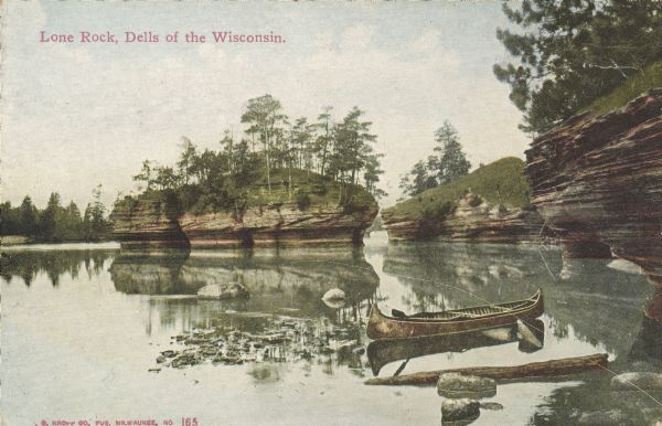Text on front reads: "Lone Rock, Dells of the Wisconsin." A canoe in the shallow water near the shore. In the distance are rock formations and islands in the river, with trees and foliage growing on the tops.