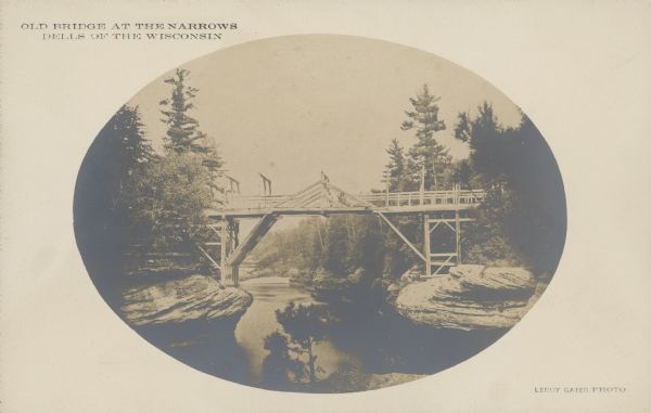 Text on front reads: "Old Bridge at the Narrows. Dells of the  Wisconsin" and "Leroy Gates Photo." The Dell Bridge, first to span the Wisconsin River, was built in 1850. Trees and formations are on both shores.