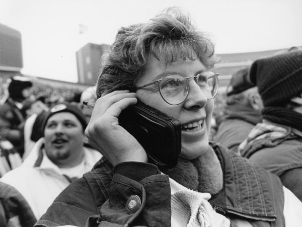 Kay Hren speaking with her husband on an early model cell phone. Photograph taken at Green Bay Packers game.