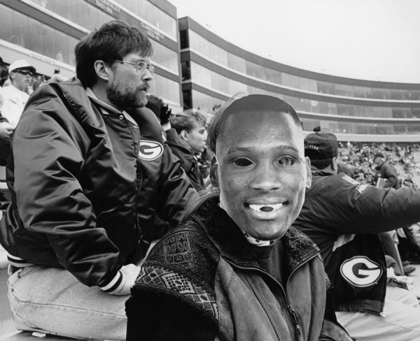 Green Bay Packer fans were given Robert Brooks masks to honor the Green Bay Packer player at this game. Brenda Wilz wears one in this photograph.