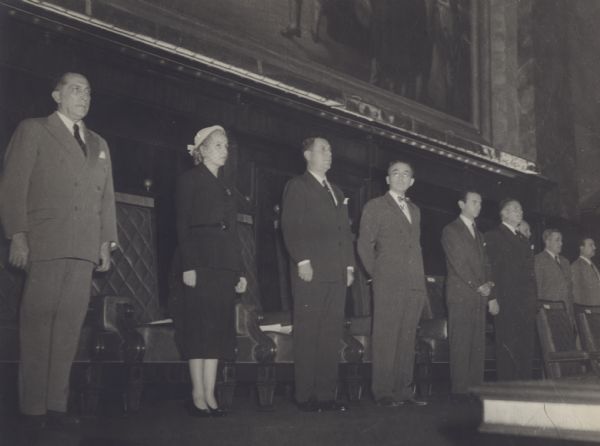 View of group of people standing on stage at the Inter-American Conference on Social Security. Arthur J. Altmeyer stands in the middle. Eva Peron stands second from left.