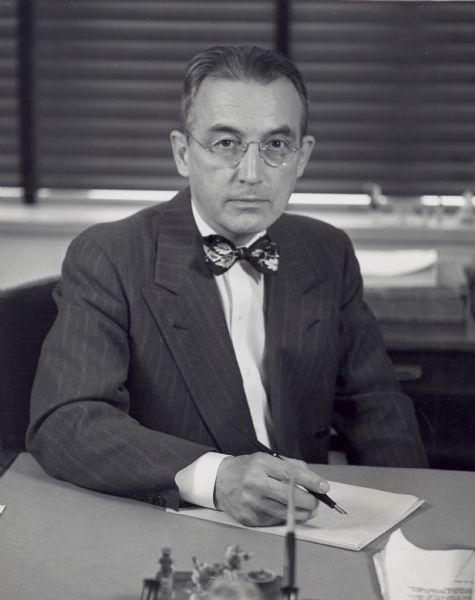 Arthur Altmeyer, seated at his desk holding a pen, gazes into the camera on his last day in office as Commissioner of Social Security.