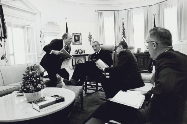 Wilbur J. Cohen is with President Lyndon Johnson and two others of the President's economic advisors in the Oval Office of the White House.