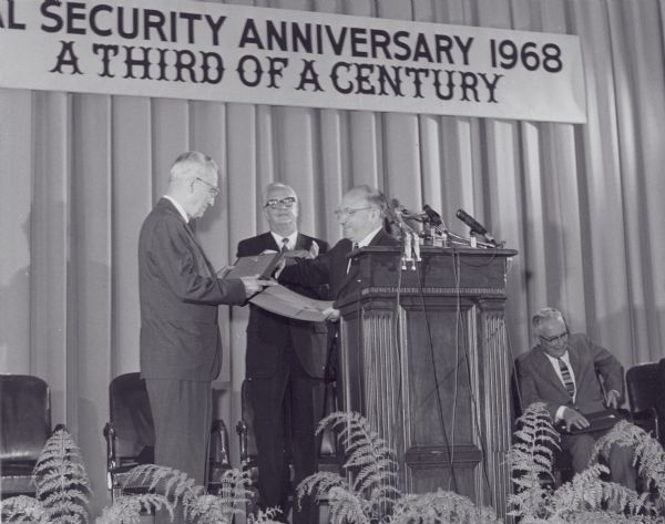 View towards podium of Wilbur Cohen presenting Arthur Altmeyer, the first director of the Social Security Board, with a plaque at the anniversary celebration of "a third of a century" of the social security bill.