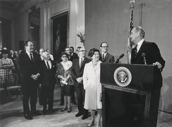 President Lyndon B. Johnson, at the podium, announces the promotion of Wilbur J. Cohen to Secretary of Health, Education and Welfare. Among the group are Wilbur's wife, Eloise, his three sons, and Vice President Hubert Humphrey. The Social Security office was part of Cohen's responsibilities as Secretary of Health, Education and Welfare.