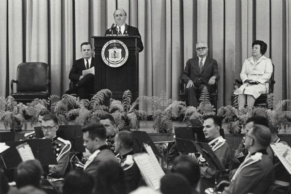 Wilbur J. Cohen stands at the podium during his swearing-in as Secretary of Health, Education and Welfare. Seated on the stage with him are his wife Eloise Cohen, Robert Ball and Donald Simpson. The Social Security office was part of Cohen's responsibilities as Secretary of Health, Education and Welfare.