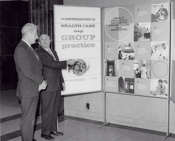 Wilbur J. Cohen, Secretary of Health, Education and Welfare, discussing a poster board about comprehensive health care with an unidentified man.