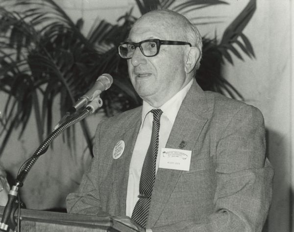 Wilbur Cohen speaks from a lectern at the 50th anniversary celebration of Social Security. On one lapel he is wearing a button which says:  "Happy Birthday! Social Security 50 years!" On the other lapel is a name tag which reads: "Social Security 50th Anniversary 1935-1985 Wilbur Cohen." Above the name tag is a pin which has a large '50' printed on it.<p>Wilbur Cohen was a research assistant with the committee which drafted the Social Security Act in 1934. He maintained an expertise and enthusiasm for public welfare throughout his career. He became Assistant Secretary for Legislation of Health, Education and Welfare in 1961. In 1965, President Lyndon B. Johnson promoted him to Under Secretary. In 1968, Cohen became the U.S. Secretary of Health, Education and Welfare.