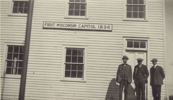 Three men are posing outside of the First Wisconsin Capitol. The man standing in the middle is C.L. (Neal) Harrington.