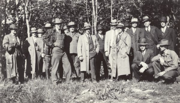 Group of men standing in a wooded area. Many are wearing suits, hats and topcoats. This is most likely at a meeting of the Association of State Foresters. The verso is inscribed: "Compliments of D.S. Burgett."
