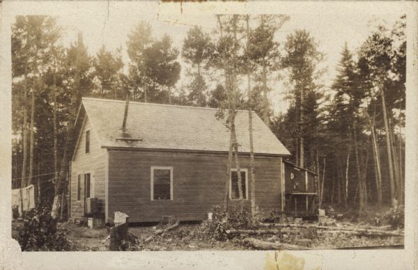 This building was used for cooking and eating. The clothesline on the left has clothes hanging on it. Neal Harrington has written on the postcard:<p>"Trout Lake. First structure erected here. Also first in Wisconsin forestry program. Built in winter-spring of 1910-1911. Cooking and eating place. Men slept upstairs if they liked that better than tents."