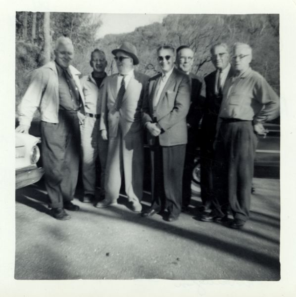 Seven men are posing outdoors for a snapshot: from right to left: Mink, Gustaveson, Nelson, Bently, Williams, Carpenter, Harrington.