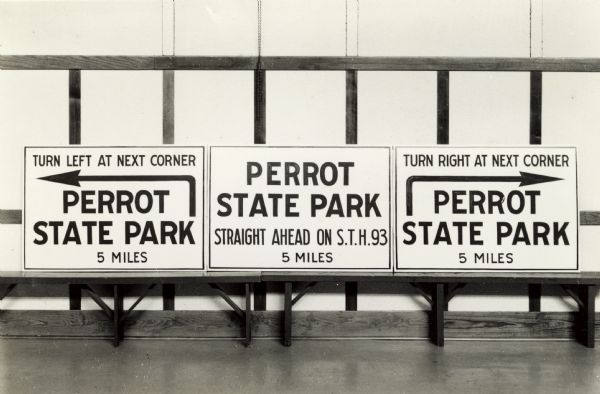 Three different signs with directions to Perrot State Park are lined up on a bench.