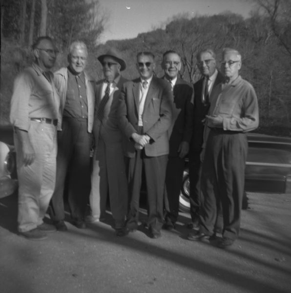 Seven men posing outdoors in front of automobiles. Left to right: Carpenter, Harrington, Williams, Bently?, Nelson, Gustaveson, Mink.