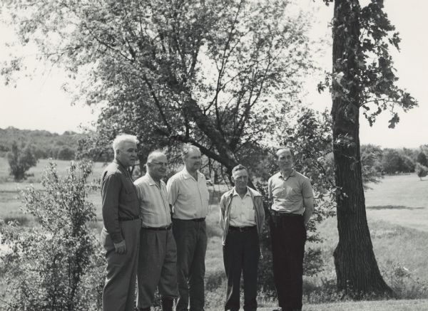 Neal Harrington and four unidentified men stand in a wooded area near an open meadow.