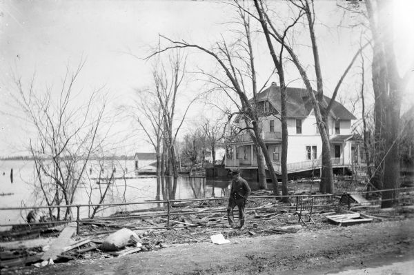 A man walks through debris along a metal railing at Cottonwood Villa after an ice storm. The lake, with houses and trees along the shoreline are in the background.