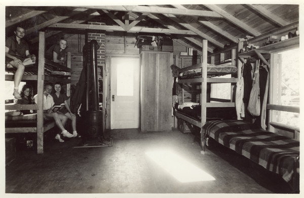 Interior view of one of the "living cabins" with several campers relaxing on bunk beds. Original caption notes: "Note spaciousness, comfortable bunks, ample storage space, weather-proof ventilation, and substantial construction."