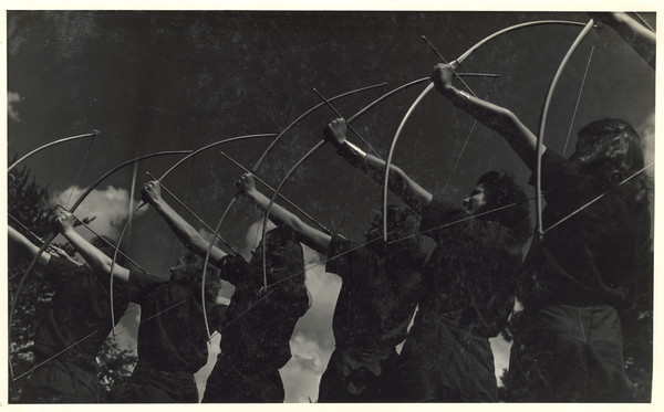 Row of six posed campers in archery stance with arrows loaded in their bows pointed towards the sky. Original caption notes: "Our three most popular Land Sports are Tennis, Archery, and Baseball.... Every activity in camp is directed by a counselor especially trained, and the campers all realize and make the most of the opportunities which The Joy Camps offer for learning or improving on, all sports skills. Our equipment is excellent, instruction and cooperation of the VERY best."