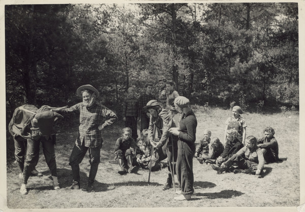 Scene from pageant, with many campers in costume acting out the story of Paul Bunyan. The group is posed sitting and standing outdoors in a sunny, grassy area adjacent to woods. The camper portraying Paul Bunyan, and the two campers portraying the ox, are on the left. A camper in the middle is on crutches. Original caption notes that this was an original play. The caption goes on to read: "It was an excellent piece of work and reflected great credit on our campers and counselors."