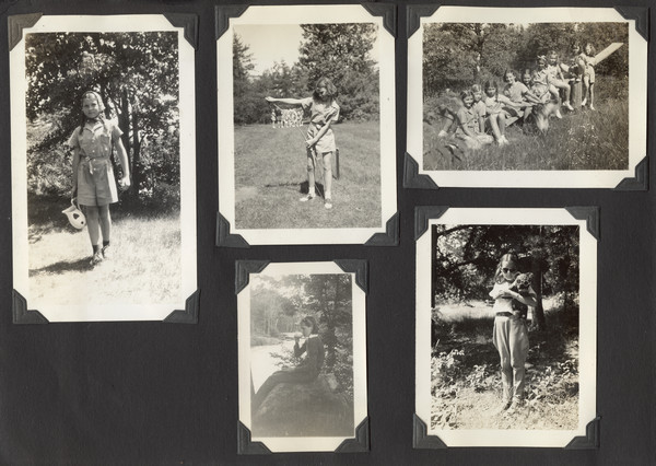 Page from Joy Camps photo album displaying five photographs. Young campers are captured in various activities, all near wooded areas. One camper in one photograph is holding a stuffed animal; both the camper and the toy are wearing sunglasses. Another camper is bending a bow for archery. Another photograph has a number of campers sitting on a seesaw; some of the campers are petting a dog. Original caption notes that these younger campers were part of Joy Camps "Camp Pioneer."