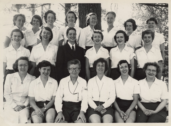 Outdoor group portrait of Joy Camps staff (undated). Camp owner and co-director, Barbara Ellen Joy, is seated front row, third from the left, with co-director Marjorie Camp immediately to her left. Original caption notes that here are "... the Leaders or Counselors for the past year. Please look at this picture with careful discrimination, for one of the important features our Camp is famous for is the background, calibre and fineness of its staff." Back of photograph carries stamp: "Minocqua Photo Shop, Victor A. Hendrickson, Minocqua, Wis."