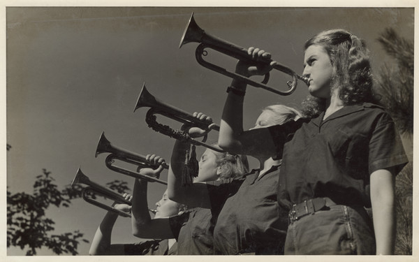 Four campers in uniform stand in a line, each holding a bugle to their mouth. Original caption notes: "These buglers are sending an urgent call for YOU to come to The Joy Camps!!!!!"