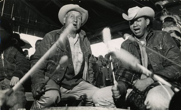 Harry Funmaker (left) of Wisconsin Dells, and Ray Tahawah of Lawton, Oklahoma, drumming. A crowd of young people is in the background.