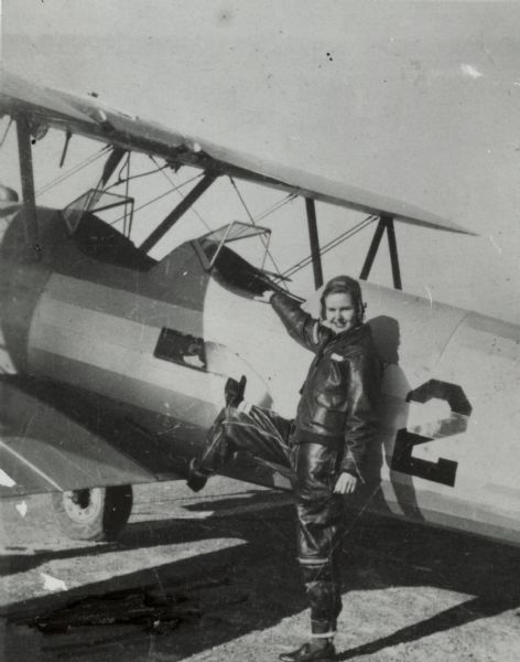 Dorothy Mosher climbing into a biplane. She is wears leather pants and a jacket.