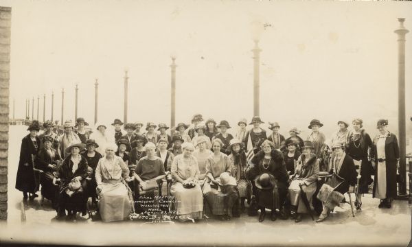 Group portrait of the Suffragette Council at the Washington Hotel. The women are gathered on a large patio lined with street lamps. Jessie Jack Hooper is in the second row at center.