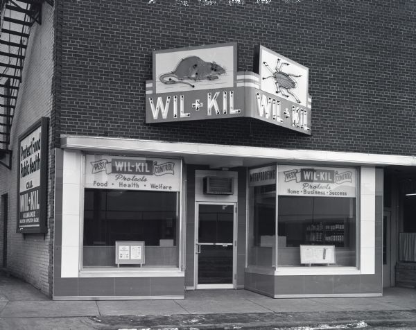 Exterior view of the Wil-Kil Pest Control building at 705 Williamson Street. The sign above the entrance features a rat and a cockroach depicted in neon.