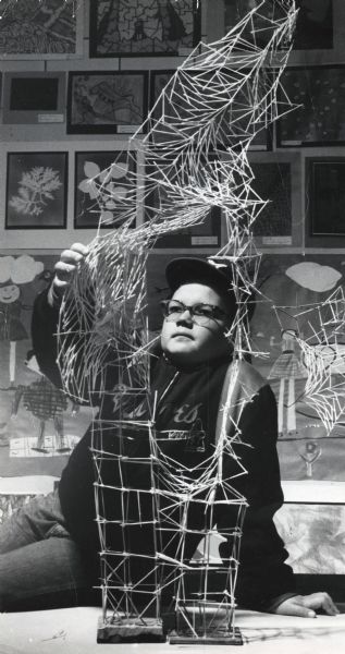 Kenneth Mills, 10, with his toothpick sculpture that he named "Pickalator." The work was part of an exhibit of children's art at Racine's Wustum Museum of Fine Arts. Mills is wearing a Milwaukee Braves cap and jacket.