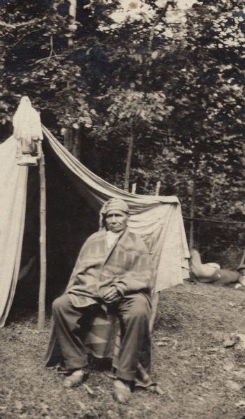 John Nuwi wrapped in a blanket and seated in a chair in front of his summer tent at Skunk Hill..