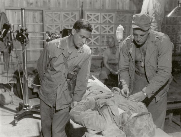 Two medics tend to a wounded soldier laying on a cot at a field hospital at Okinawa.