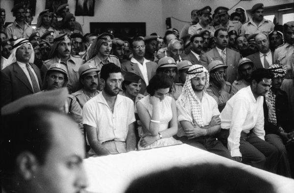Man and woman seated in the front row of a court room, one or both of them on trial for treason in Jordan. The room is crowded with primarily men, many in military uniform.