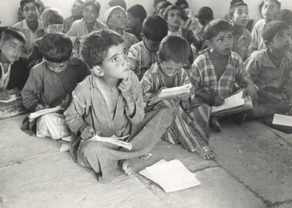 Group of boys seated on the floor of a school with paper and pencils. The school was built with U.S. aid.